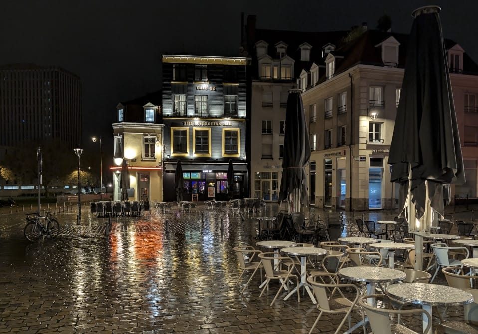 Terrasses et pavés mouillés devant le Café Oz, un soir de pluie à Lille